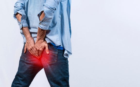 Čovek drži ruke na zadnjici jer ima problema sa analnom fistulom.